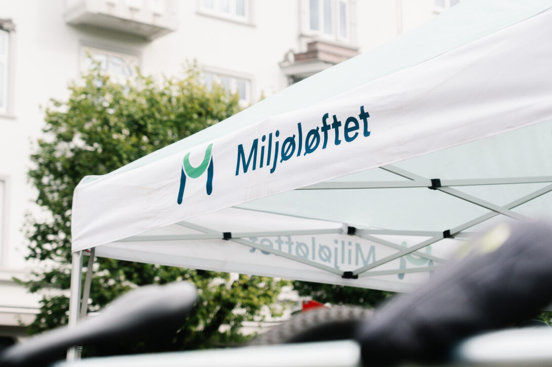 Miljøløftet-logo trykket på et hvitt partytelt satt opp utendørs under Bilfri dag, med bygninger og trær i bakgrunnen.