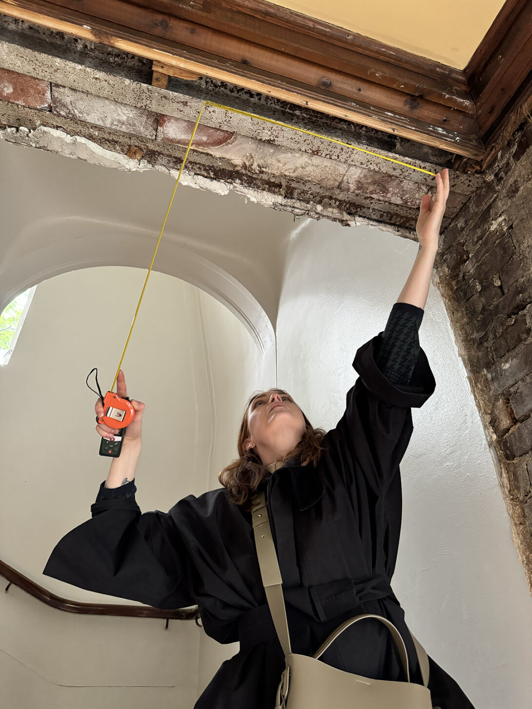 En kvinne måler takhøyden med målebånd under befaring i et rom under renovering.